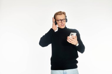 Kulaklık takan genç yakışıklı bir adam akıllı telefonuyla dikkatle müzik dinliyor..