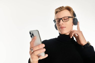 Gözlüklü genç bir adam müzik dinler ve akıllı telefonuyla rahatlar..