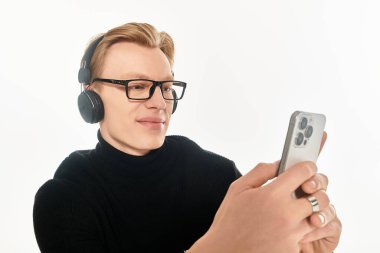 Gözlüklü gülümseyen genç adam akıllı telefon ekranına odaklanırken müzik dinliyor..