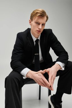 Gösterişli siyah takım elbiseli kendine güvenen genç adam minimalist bir stüdyoda parlak bir görünüm sergiliyor..