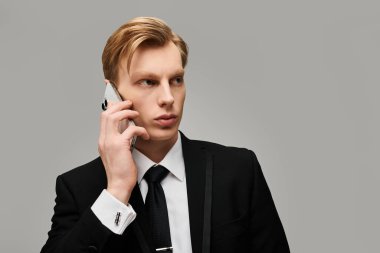 Sivri takım elbiseli genç ve yakışıklı bir adam bir telefon konuşmasına odaklanmış, düşünceli görünüyor..