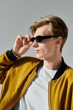 Genç ve yakışıklı bir adam güneş gözlüklerini düzeltirken modaya uygun kıyafetlerini ve kendine güvenen tavırlarını sergiliyor..
