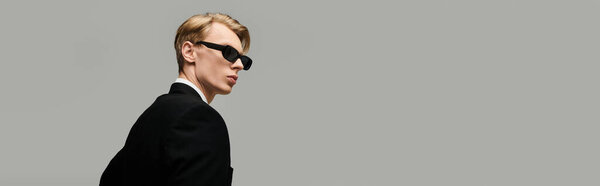 Stylish young man wearing sunglasses poses confidently, showcasing a modern and sophisticated look.