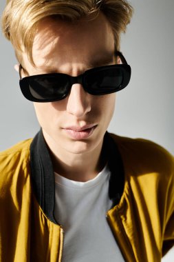 A young handsome man gazes confidently while wearing sunglasses and a trendy bomber jacket. clipart