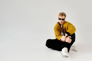 Güneş gözlüklü şık bir genç adam modern modanın altını çizerek şık bir ortamda rahatlıyor..