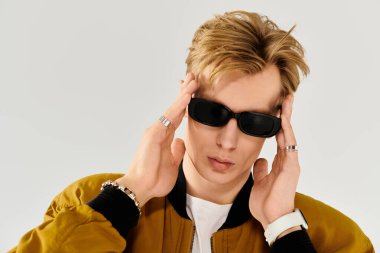 Şık görünümlü genç bir adam, kendine güvenini ve tarzını gösterirken güneş gözlüğünü ayarlıyor..