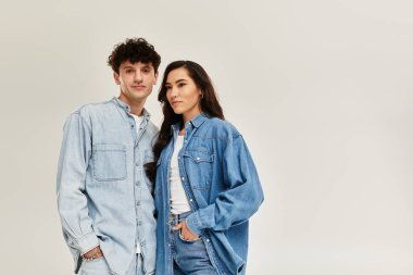 Genç ve şık bireyler, şık kot kıyafetleriyle yumuşak bir zemine karşı güvenle duruyorlar..