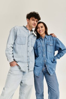 Genç bir çift eşleşen kot kıyafetlere güvenir, gülümser ve kapalı alanda birlikte poz verir..