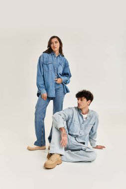 Two stylish individuals in trendy denim outfits pose elegantly in a minimalistic studio environment. clipart