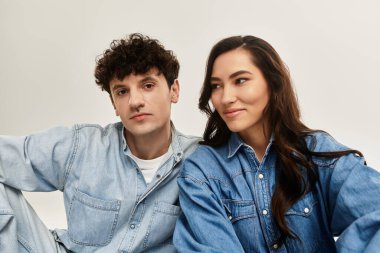 A young couple poses in trendy denim outfits, exuding confidence and style in a minimalist studio. clipart