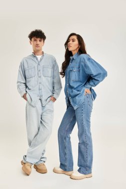 Genç, modaya uygun bir çift şık kot giysileri ve şık bir havayla ayakta duruyor..