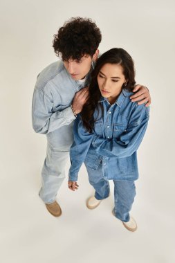 Modaya uygun kot giyimli genç çift, minimalist bir stüdyo ortamında birlikte poz veriyorlar..