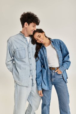 Genç bir çift neşeli bir anda kucaklaşıyor, modern uzayda moda kot kıyafetlerini sergiliyorlar..