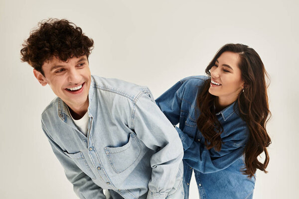 Два модных человека разделяют радостный смех, одетые в координированные джинсовые наряды.