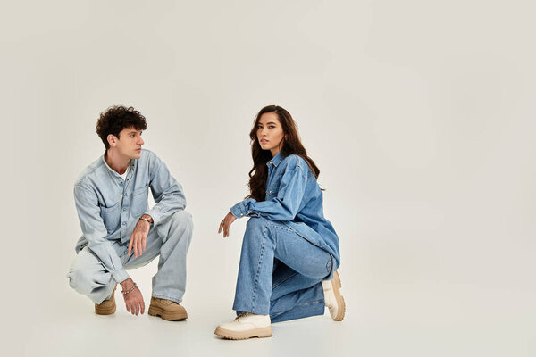 Two stylish individuals pose in trendy denim outfits against a soft backdrop.