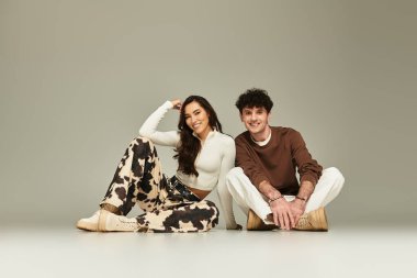 İki modaya uygun genç, yerde neşeyle poz veriyor, özgüven ve tarz yayıyorlar..