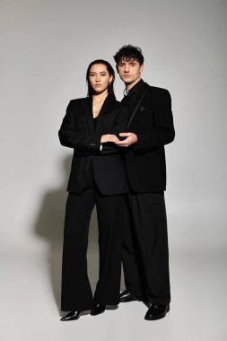 Moda kıyafetleri içinde genç bir çift, hafif ışıklandırmalı minimalist bir stüdyoda güvenle duruyor..