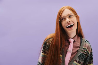 Uzun kızıl saçlı genç bir adam mor bir arka fona karşı şık bir şekilde poz verir..