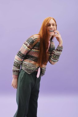 Uzun kızıl saçlı genç bir adam, modaya uygun giyinip, tarzını sergilerken parlak bir şekilde gülümsüyor..