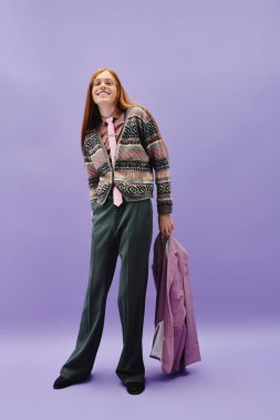 Uzun kızıl saçlı şık bir genç adam mor bir arka plana karşı güven içinde poz verir..