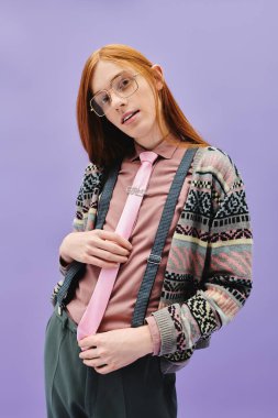 Uzun kızıl saçlı genç bir adam, mor bir arka fona karşı şık bir elbiseyle güven içinde poz verir..