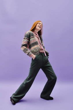 Genç, eşcinsel bir adam mor bir arka plana karşı şık kıyafetler içinde poz verir..