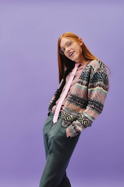 Uzun kızıl saçlı genç bir adam şık elbisesini sergiliyor. Kendine güveni ve cazibesi tam..