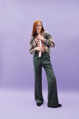 Uzun kızıl saçlı yakışıklı genç bir adam gülümserken şık görünüşünü sergiliyor..