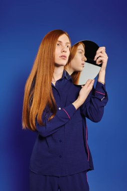 Uzun kızıl saçlı şık bir genç adam zarif poz verirken kimliğini yansıtır..