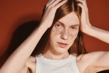 A young queer man with long red hair and freckles showcases a stylish look against a bold backdrop. clipart