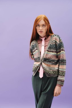 Kızıl saçlı genç bir adam yaratıcı bir stüdyoda poz verirken şık kıyafetlerini sergiliyor..