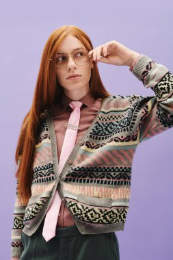 Kırmızı saçlı şık bir genç adam, mor renkli bir hırka ve pembe kravat takıyor..