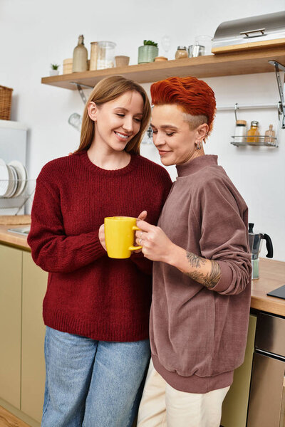 В уютной современной квартире за ярко-желтой чашкой улыбается красивая пара.