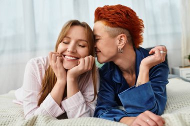 İki güzel genç kadın, modern yatak odalarında kucaklaşırken aynı şefkatli gülümsemeyi paylaşıyor..