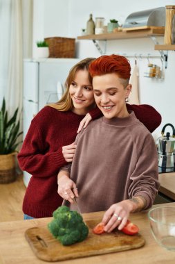 İki genç kadın, modern dairelerinde birlikte yemek pişirirken neşe ve kahkaha paylaşıyor..