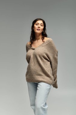 Gri arkaplanda, rahat bej bir süveterin içindeki güzelliği ve güveni kucaklamak.