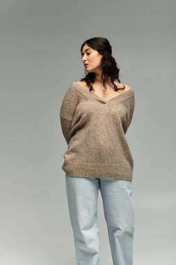 Güzel, genç, iri yarı, rahat bej kazaklı bir kadın stüdyoda zarif pozlar veriyor..