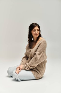 Gri bir arka planda rahat bej bir süveterin içindeki güzellik ve güveni kucaklamak.