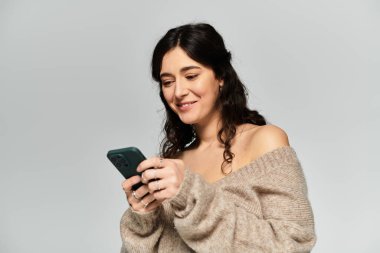 Esmer kadın, gri bir arka planda yumuşak bir gülümsemeyle stüdyoda vakit geçirmekten hoşlanıyor..