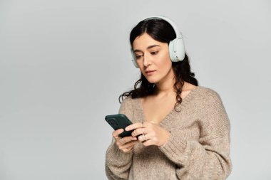 Gri bir geçmişi olan bir stüdyoda genç bir kadın telefonunda müzik dinlemekten hoşlanıyor..