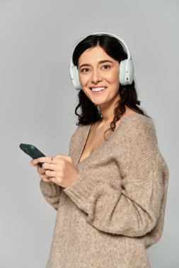 Brunette young woman smiling in casual attire with headphones in a gray studio setting. clipart