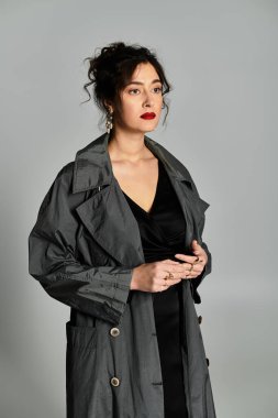 Zarif giyinmiş çarpıcı esmer kadın zarif bir şekilde gri arka plana karşı duruyor..