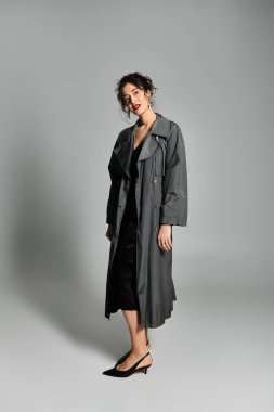 Şık giyinmiş zarif esmer kadın gri bir arka plana zarif bir şekilde poz veriyor..