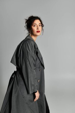 Stüdyodaki zarif genç kadın gri arka planda sofistike bir tarz sergiliyor..