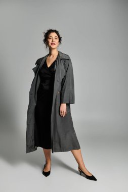 Zarif esmer kadın, yumuşak gri bir arka plana karşı şık bir şekilde poz veriyor..