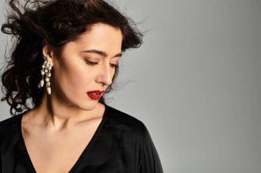 Stüdyoda zarif bir şekilde poz veren zarif esmer kadın gri zemine karşı..