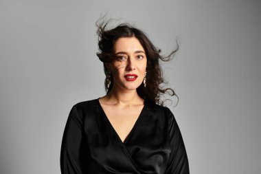 Şık siyah elbiseli zarif genç bayan stüdyoda zarifçe poz veriyor..