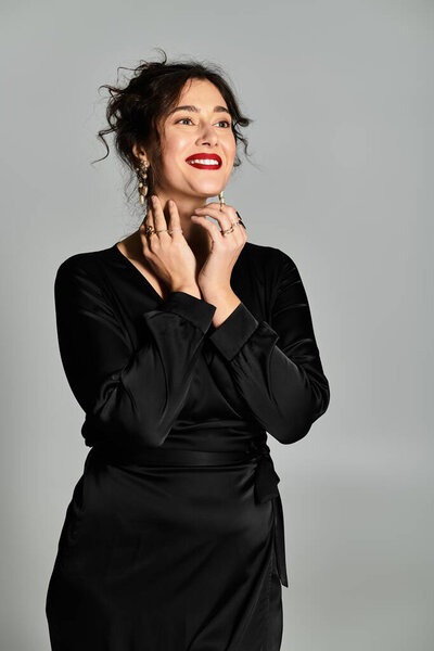 Confident plus-size woman shines in elegant black wear against a grey background.