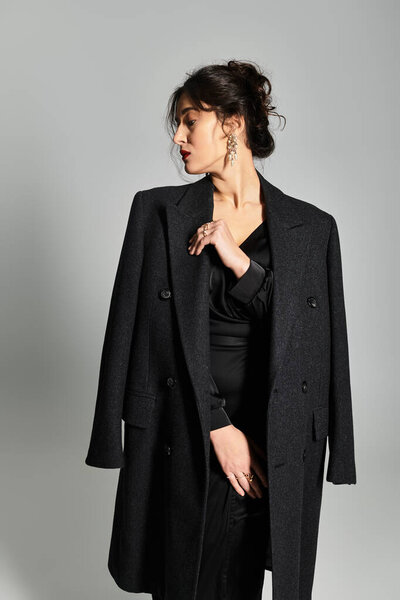 Elegant brunette woman in sophisticated attire poses gracefully in studio setting.