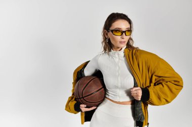 Şık giyinmiş zarif genç bir kadın elinde modern moda eğilimlerini sergileyen bir basketbol topu tutuyor..